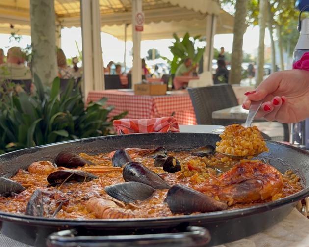 A hand scooping paella with a spoon from a vowl