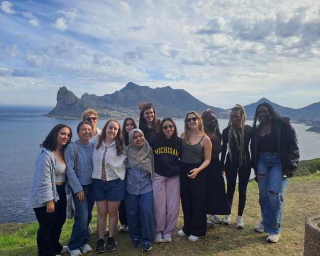 Group of students standing in front of a body of water with mountains in background
