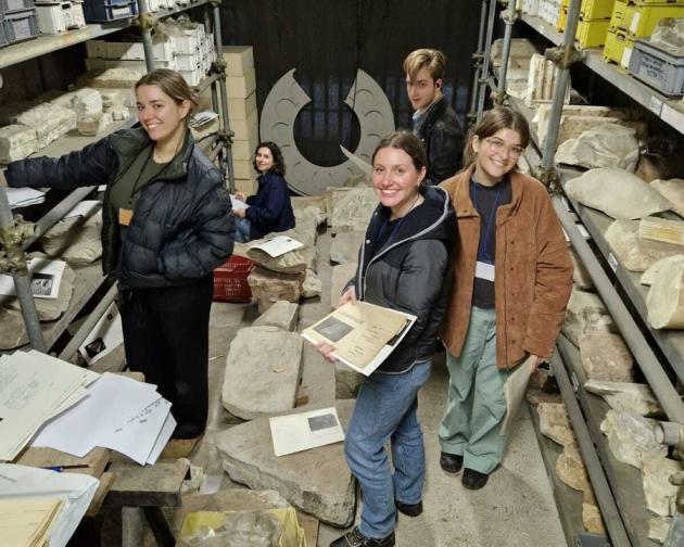Five students smiling while working with stone artifacts and documents in an archive room