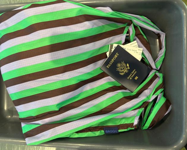 A passport laying on top of a striped bag in a TSA bin.