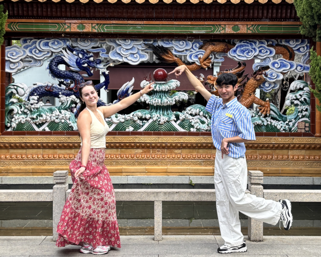 Two students smiling and posing in front of a sculpture.