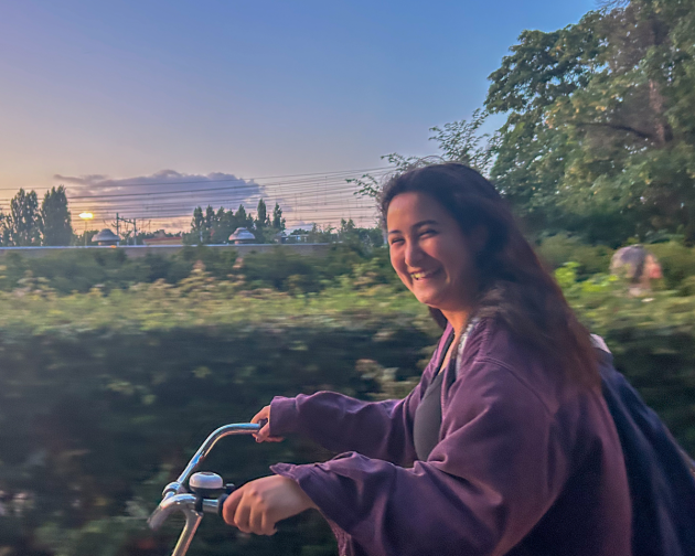 A student riding their bike and smiling with the sunsetting in the background.
