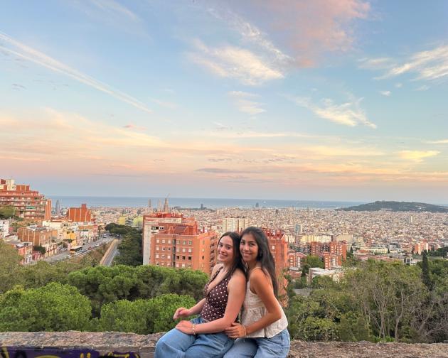 Two students smiling in front of a sunset with buildings in the background.