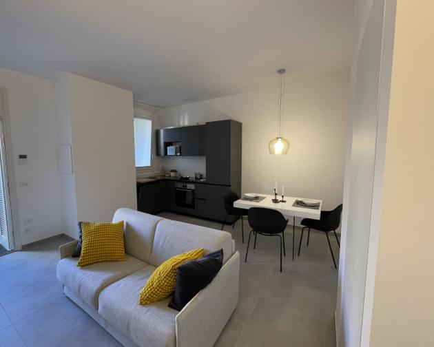 A modern apartment in Milan showing an open kitchen, dining room table, and couch.