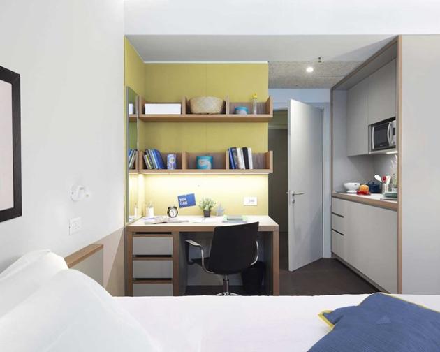 A studio apartment including a bed, desk, and kitchen area.