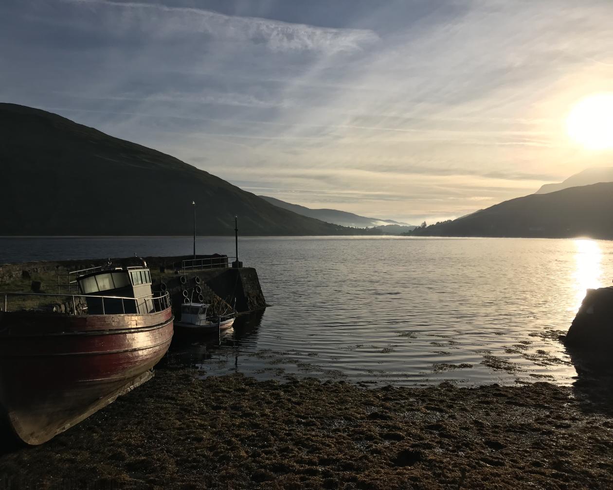 Multiple boats rest against the shore as the sun sets in Leenaun, Ireland. 