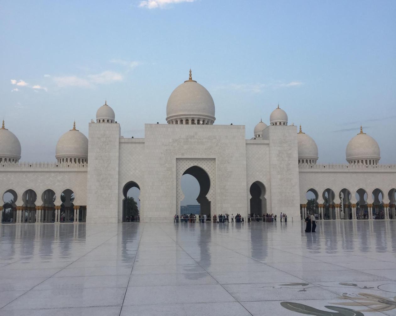 White marble mosque with domes, blue sky background. This alt text was added with Al; accuracy may vary.