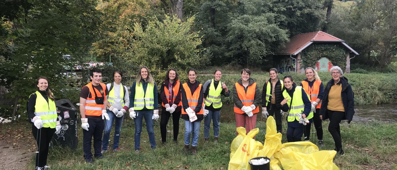 12 people wearing reflective vests standing behind a pile of full trash bags
