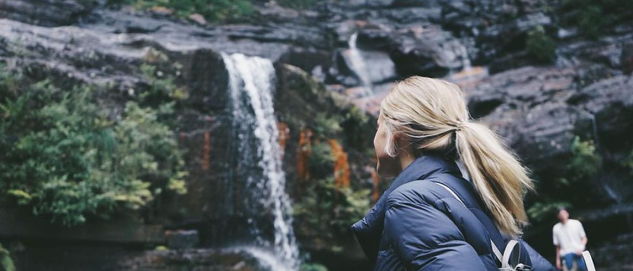 student wearing cold weather gear looking up towards a waterfall