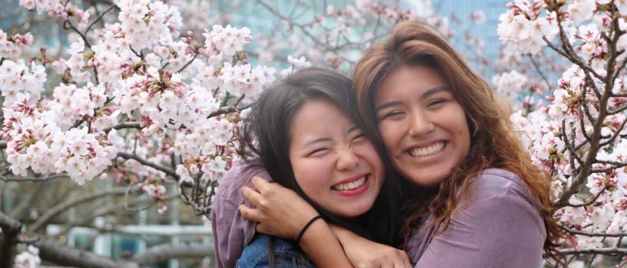 students hug and smile among the cherry blossoms in Tokyo