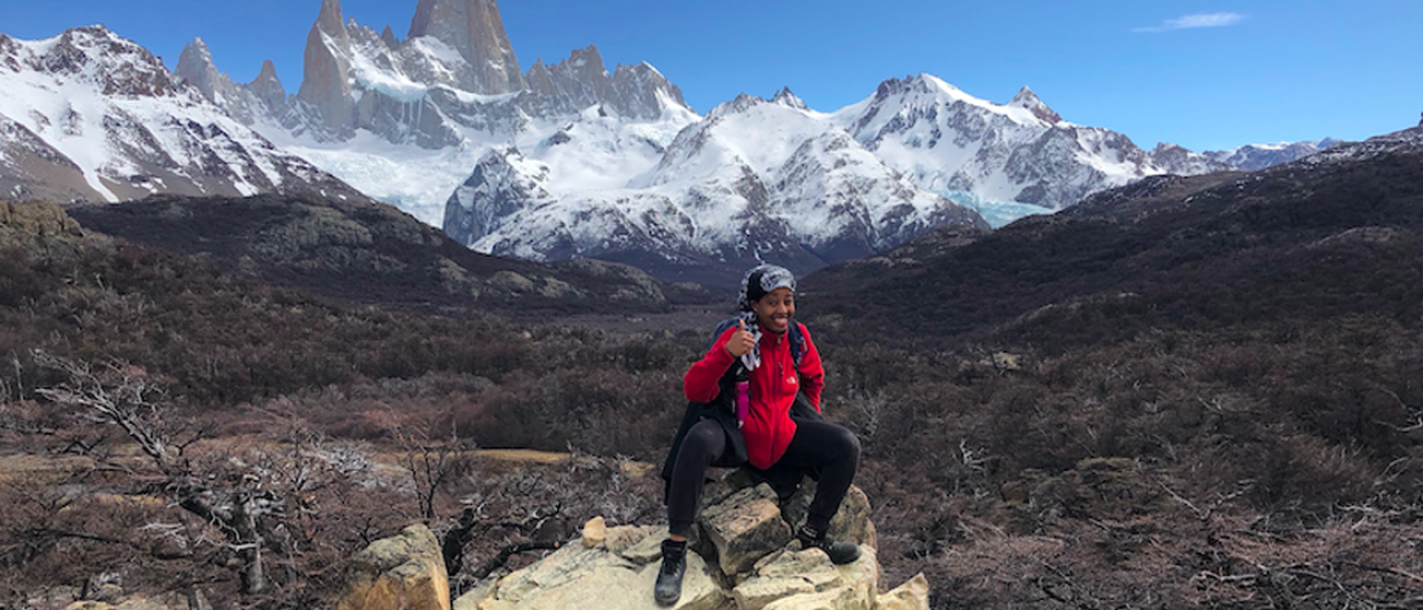 student in backpacking gear in front of snow capped mountains