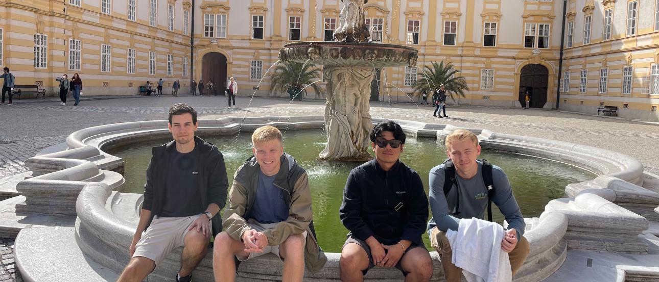 four students pose for a photo at Melk Abbey while sitting on the edge of the fountain