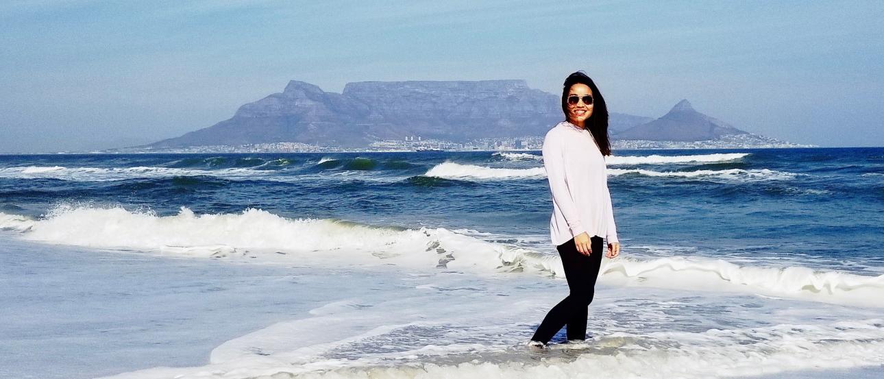 a student standing in the water in Cape Town with a mountain behind her
