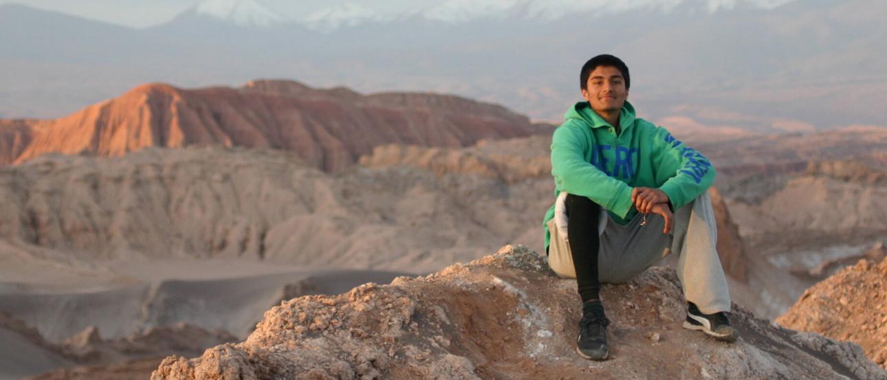 a male student sitting in Valle de la Luna in Chile with a mountain backdrop