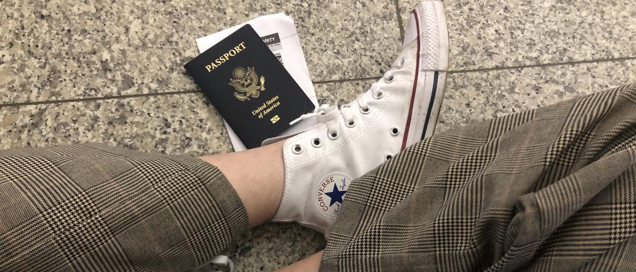 Student sits crosslegged with their passport and boarding pass in an airport