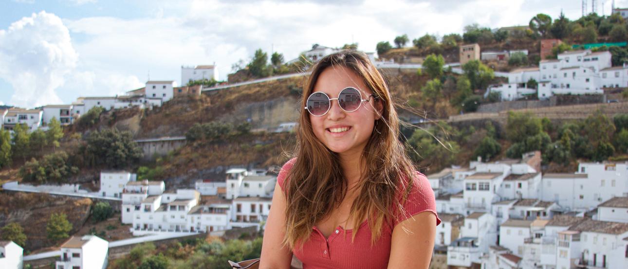 Student sits on a ledge in Granada wearing short sleeves and sunglasses