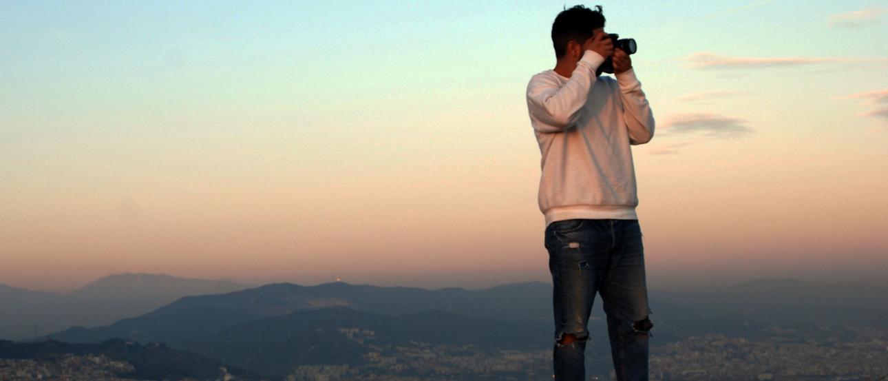a student standing cliffside taking a photo during dusk