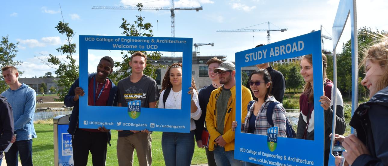 students standing on pavement near grassy area holding up square cut-out signs that read "UCD College of Engineering & Architecture"
