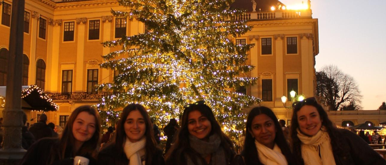 Five friends standing in front of a Christmas tree holding mugs of cocoa.