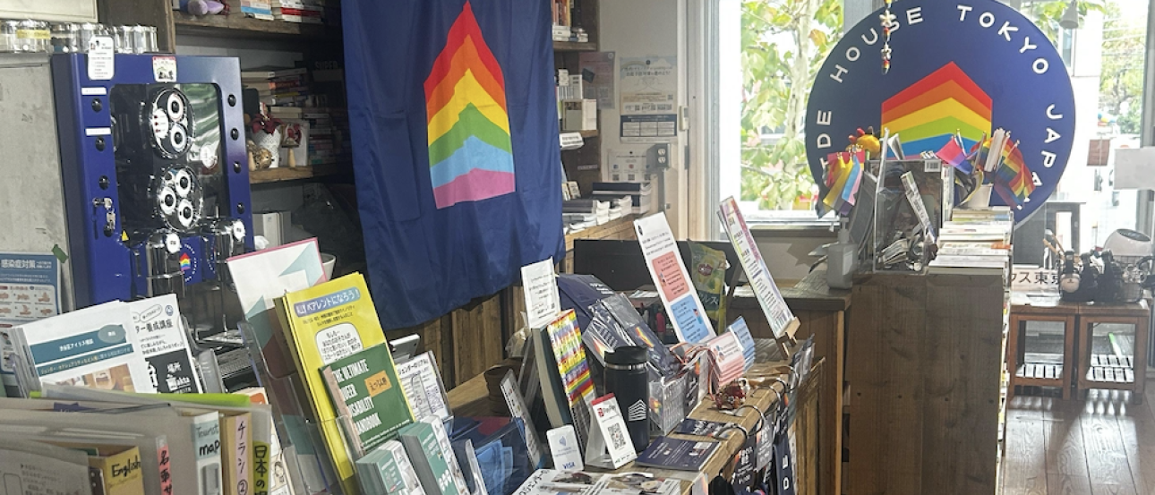 Shelves of LGBTQ books and resources with flags in the background