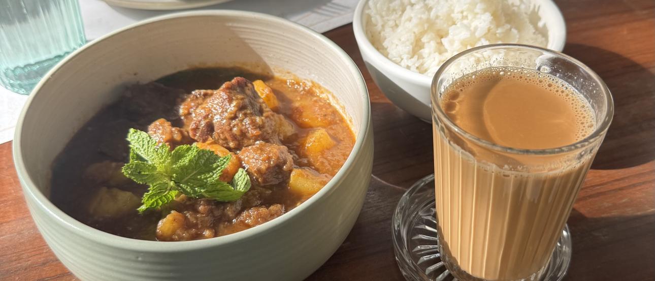 a meal consisting of a bowl of curry, a bowl of rice, and some milk tea