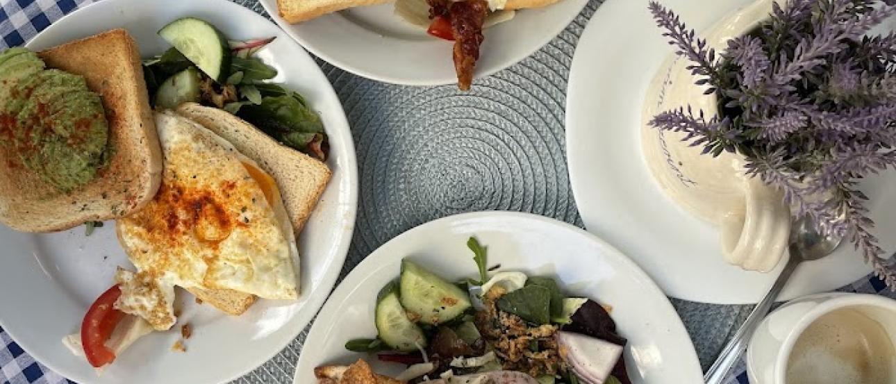 Photo from above of three plates filled with breakfast food, coffee cups, and plant on a small table