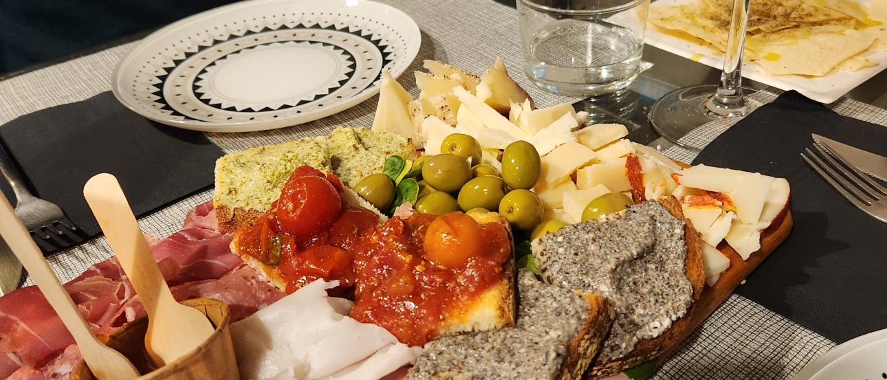 A table filled with Italian aperitivo dishes including cured meats, cheeses, olives, bruschetta, and bread, served with an Aperol Spritz at a restaurant in Milan.