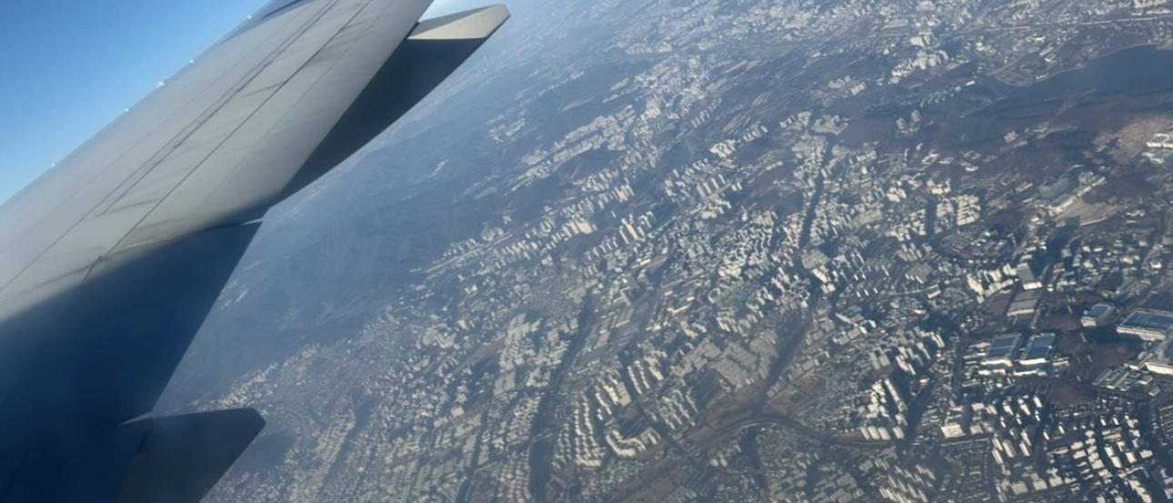 View outside of a plane window showing the Chicago metropolitan area, the right wing of a plane, and a blue sky.