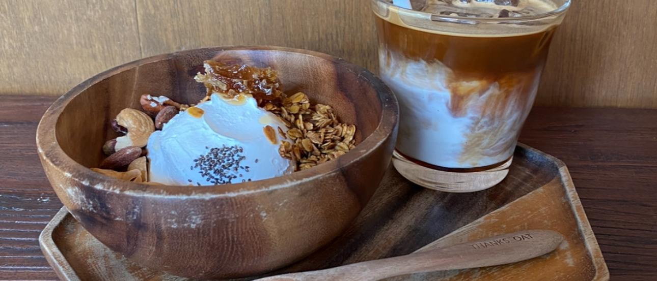A latte and a yogurt bowl with granola and honey served on a six-sided wooden tray with a wooden spoon.