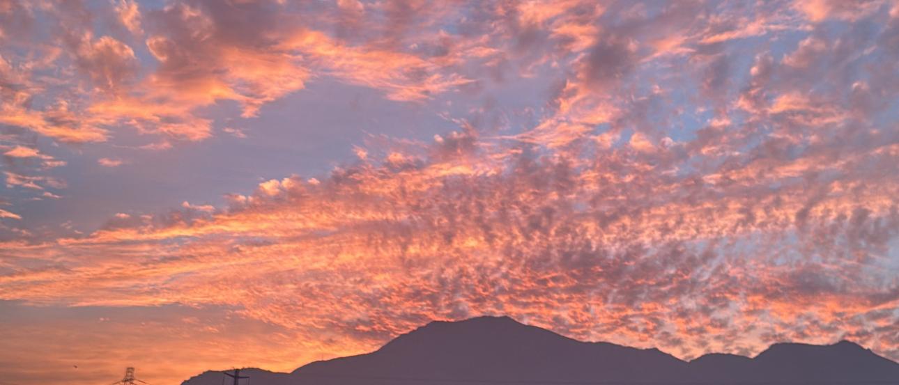 Vibrant oranges spread across the horizon and puffy clouds scatter the sky, the dark silhouette of the Andes mountains is a stark contrast to the colors.