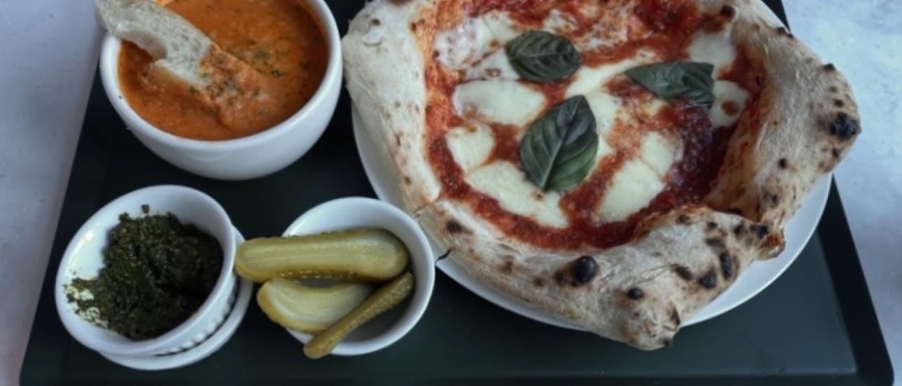 Pizza, tomato soup, and pickles on a tray.