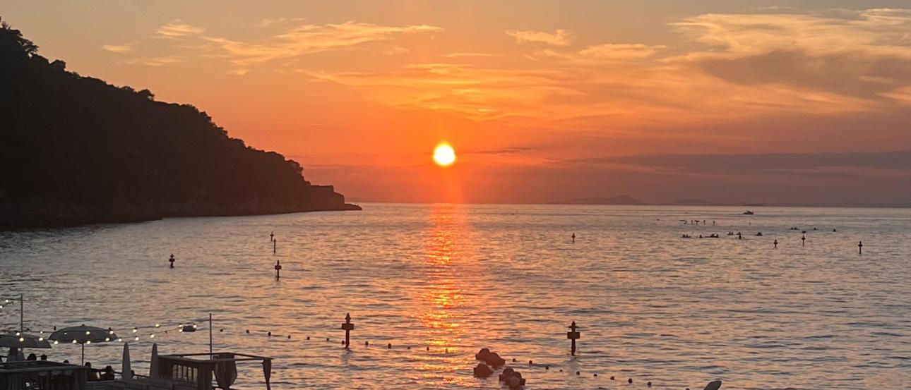 A vibrant sunset over the sea in Sorrento, Italy, with orange and pink skies reflected on the water. 