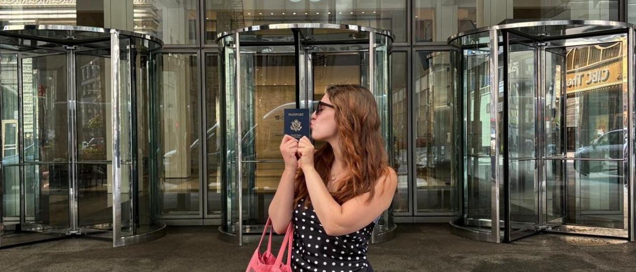 The author stands in profile, kissing the side of a passport in front of a building lobby