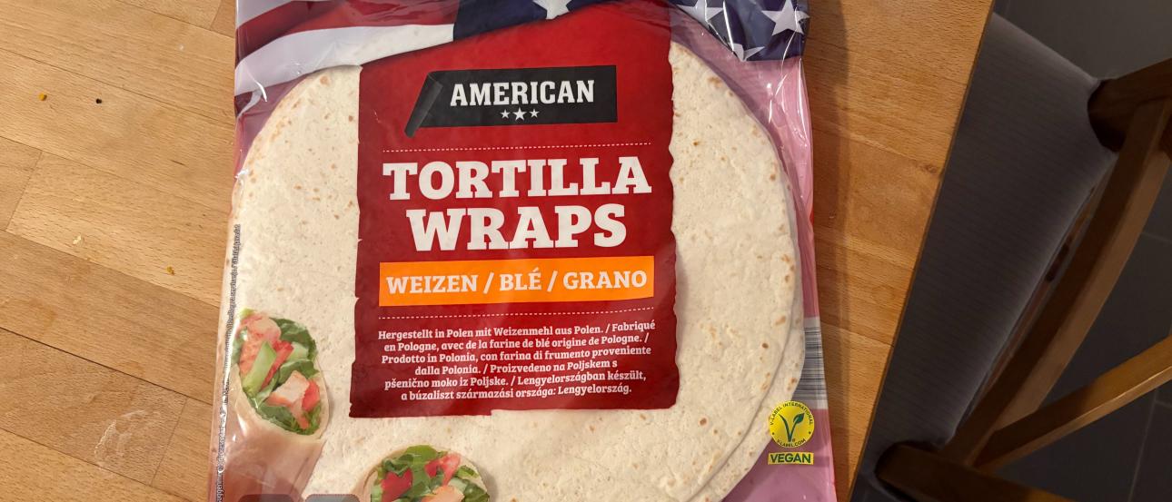 A bag of tortilla wraps labeled "American" rests on a wooden table.