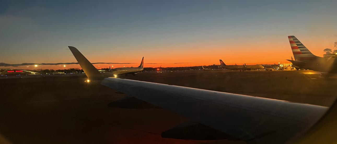 View from an airplane in Boston at Logan Airport, with the sunset and terminal visible outside.