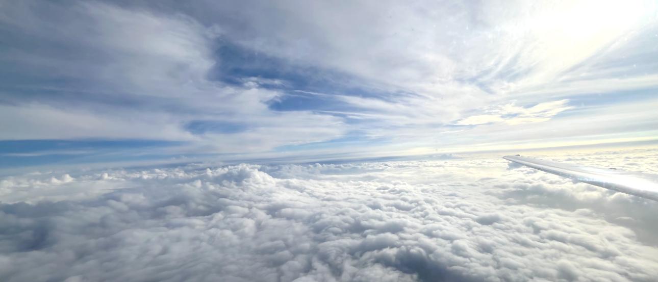 A wide shot of a blue sky covered in white clouds from the window of an airplane.