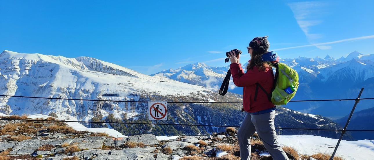 A student dressed in hiking gear takes a photo of the mountain peaks in the Alps while on a class trip from Freiburg.