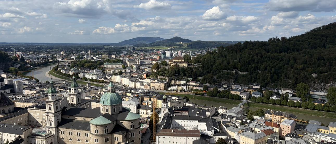 An aerial view of Salzburg, taken from the fortress. There are many houses and buildings below, including a cathedral.