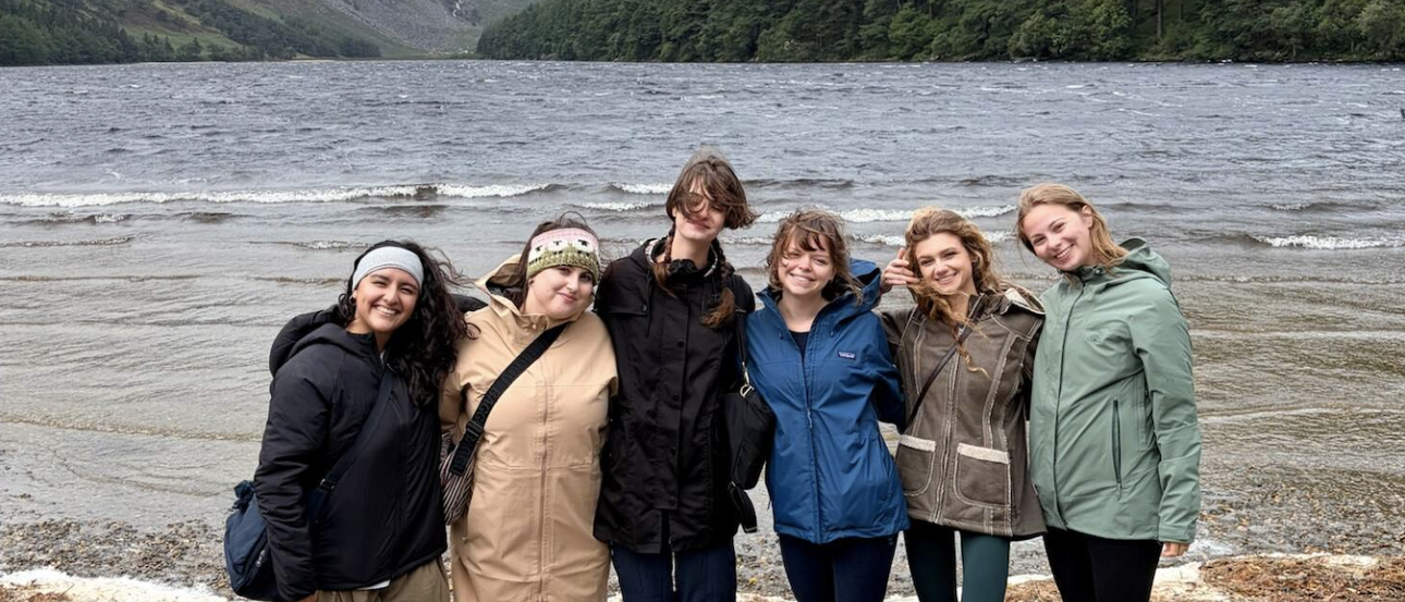 6 people pose for a photo with a body of water and green mountains in the background. 