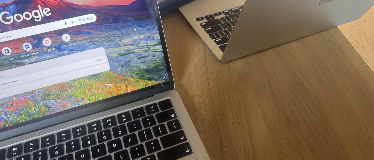 Two computers on a table sitting on a wooden table.