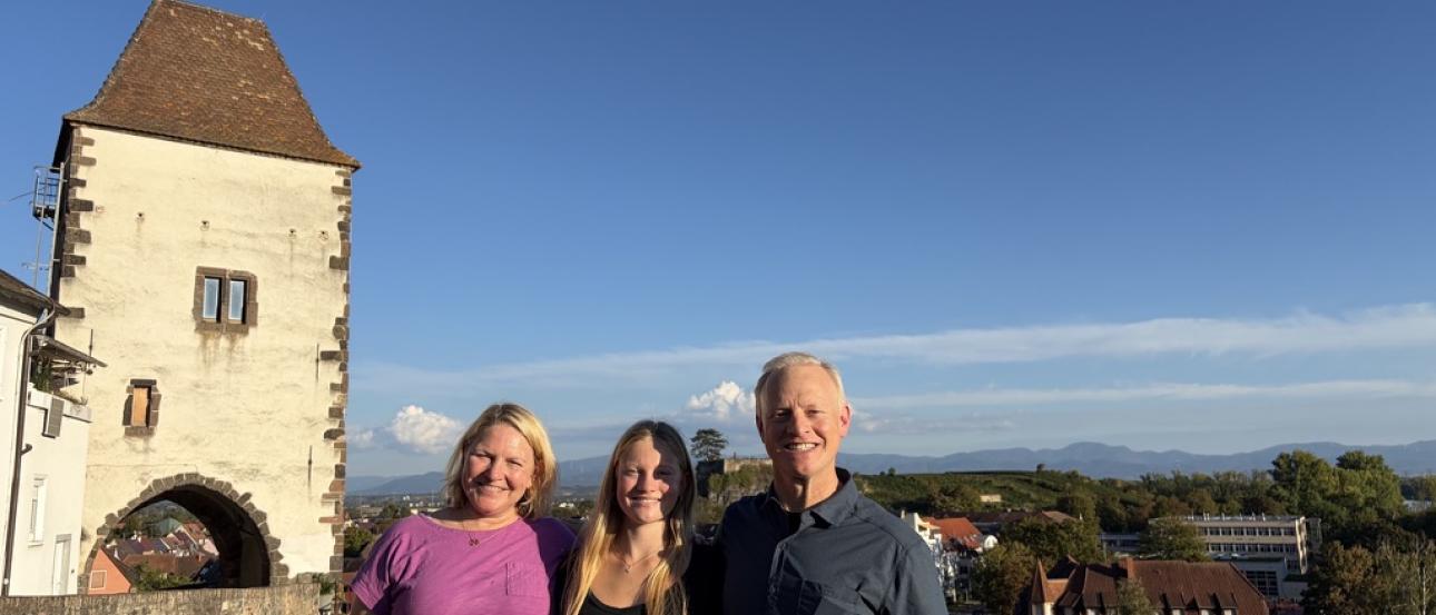 3 people stand on a hill with a castle in the background