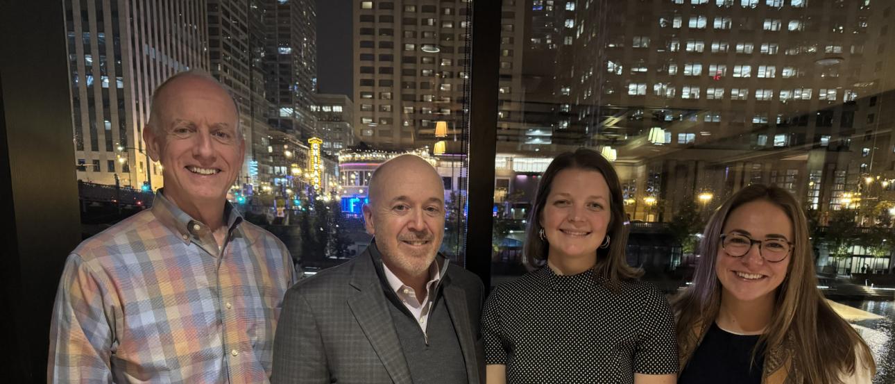 Two men and two women stand side by side in front of night skyline