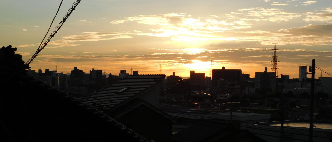Sunset over a city skyline with silhouetted rooftops and clouds. This alt text was added with Al; accuracy may vary.