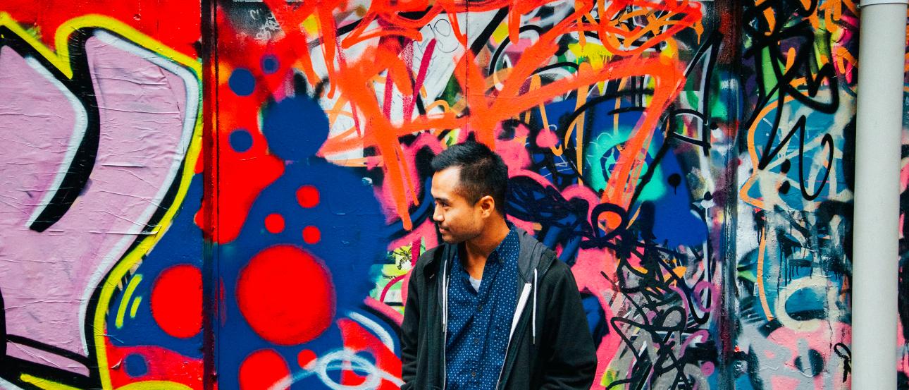 1. Hand framing distant lighthouse by the sea.
2. People walking on a plaza under a golden pavilion.
3. Person on a hill overlooking a city with tall grasses.
4. Person standing in front of colorful graffiti wall. This alt text was added with Al; accuracy may vary.