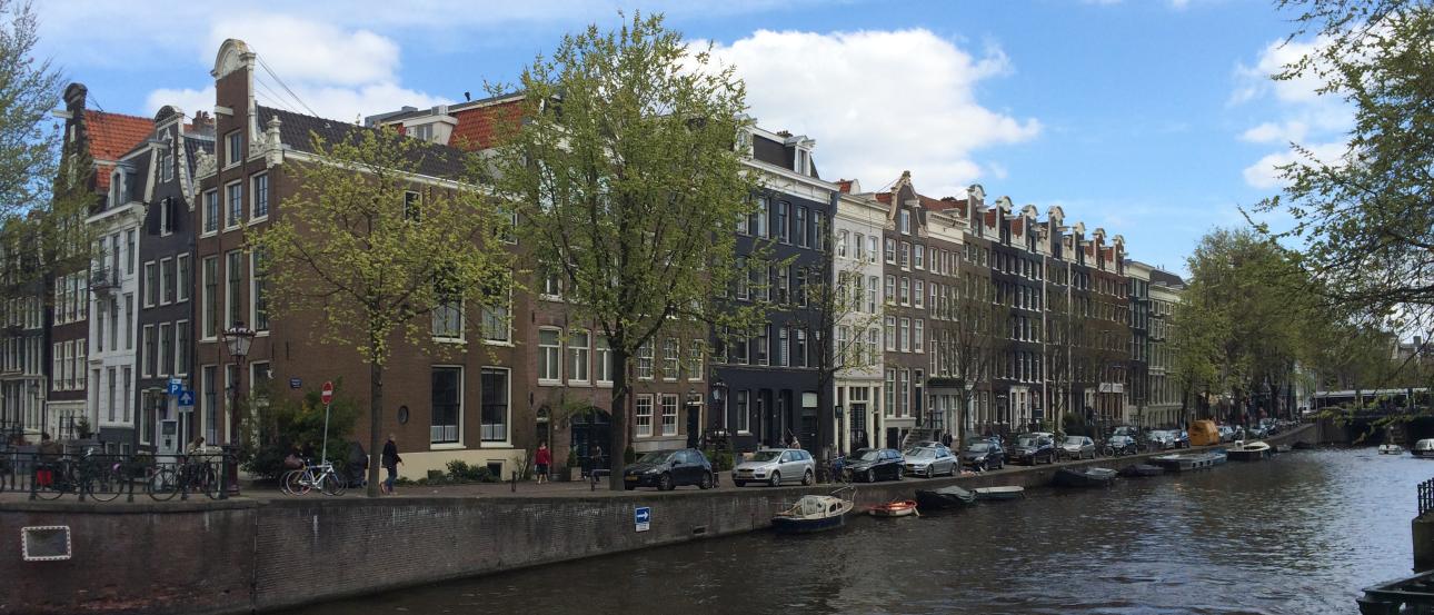 Canal with boats, lined with historic buildings and trees under a blue sky. This alt text was added with Al; accuracy may vary.