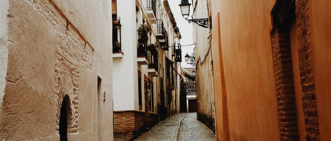 Three people smiling near ancient ruins.

Cliffs and ocean under cloudy skies.

Metal sculpture beside a brick building.

Person on a balcony with a city view at night.

Narrow cobblestone alley between buildings. This alt text was added with Al; accuracy may vary.