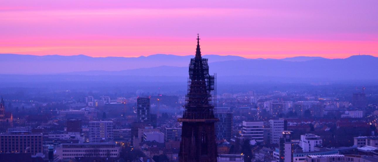City skyline at dusk with a tall spire silhouetted against a purple and pink sky. This alt text was added with Al; accuracy may vary.
