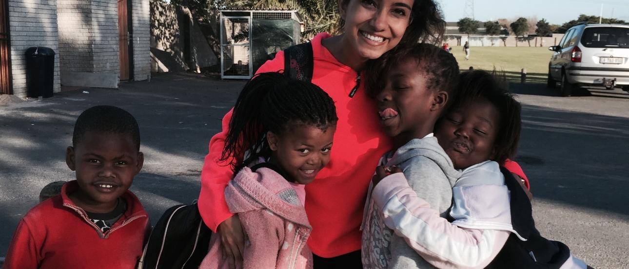 Smiling woman and four children hugging outdoors, sunny day. This alt text was added with Al; accuracy may vary.
