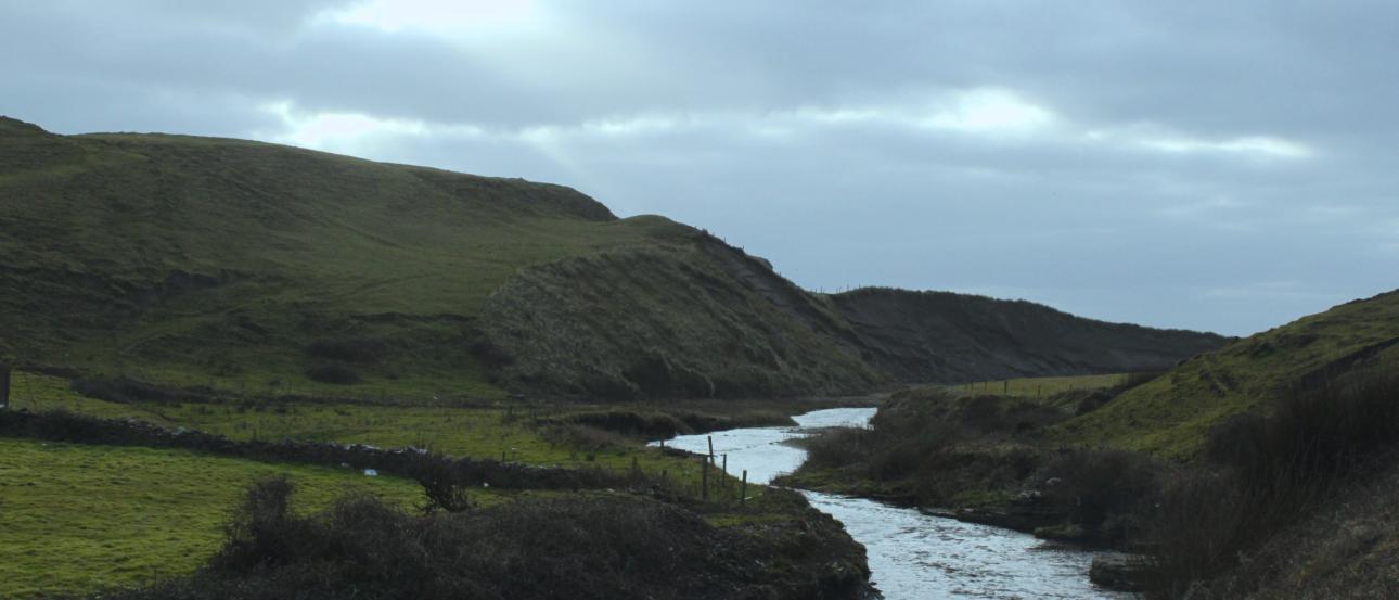 River winding through green hills under a cloudy sky. This alt text was added with Al; accuracy may vary.