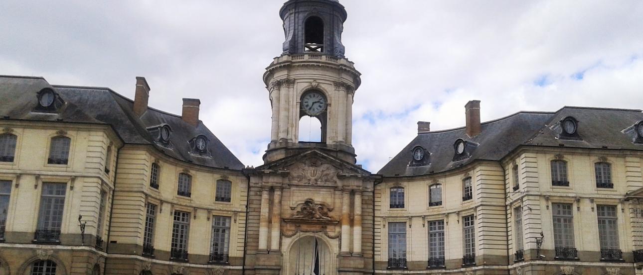 Elegant building with a central clock tower under a cloudy sky. This alt text was added with Al; accuracy may vary.